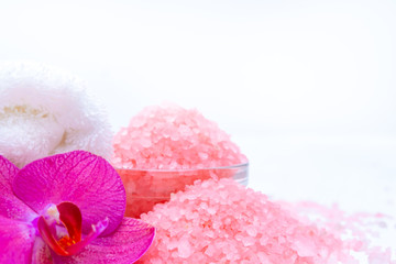 Spa cosmetic and beauty treatment concept. Pink spa sea salt, white towel and purple orchid on white wooden background. copyspase flatlay.