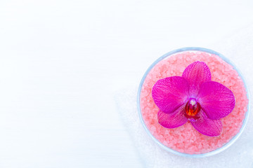 Obraz na płótnie Canvas Spa cosmetic and beauty treatment concept. Pink spa sea salt and purple orchid on white wooden background. copyspase flatlay.