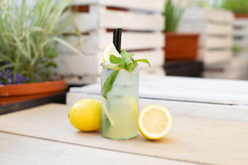 Cytrynowa lemoniada w szklance z cytrynami, miętą na tle ogródka.