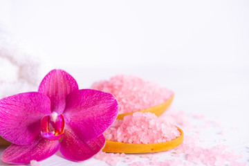 Fototapeta na wymiar Spa cosmetic and beauty treatment concept. Pink spa sea salt, white towel and purple orchid on white wooden background. copyspase flatlay.
