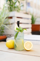 Cytrynowa lemoniada w szklance z cytrynami, miętą na tle ogródka.