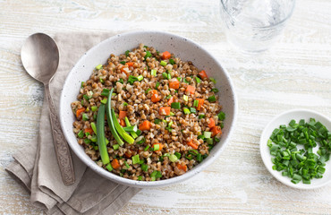 Delicious vegan buckwheat with vegetables and green onions on a light wooden background. Healthy homemade food