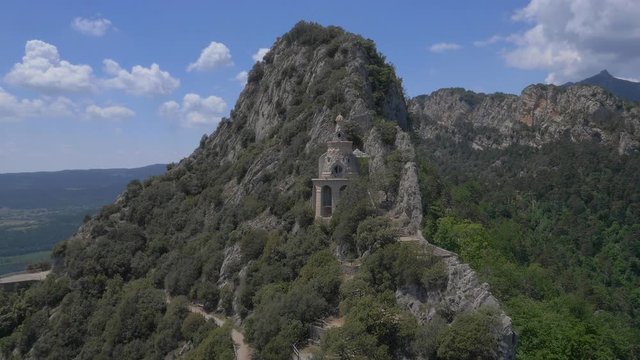 AERIAL DRONE ORBIT AND APPROACH TO RELIGIOUS CATHOLIC SANCTUARY CARVED IN THE ROCK OF MOUNTAIN RANGE AND FOREST