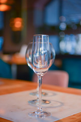 Transparent empty champagne and wine glasses on the rustic wooden table over blurred restaurant background.