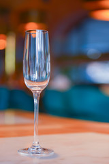 Transparent empty champagne glass on the rustic wooden table over blurred restaurant background.
