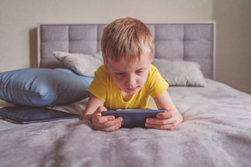 Distance education, learning. Boy is lying on the bed with a smartphone in the room. Child with a gadget. Teenage child using smartphone.