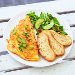 Smażone jajka, omlet, potrawa na śniadanie, biały talerz, dodatki sałatka i warzywa oraz pieczywo.