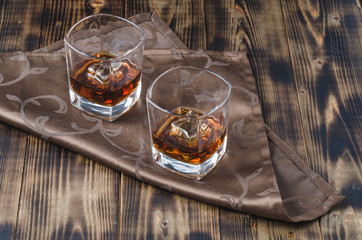 Two glasses of whiskey and ice cubes/Two glasses of whiskey and ice cubes on a napkin.