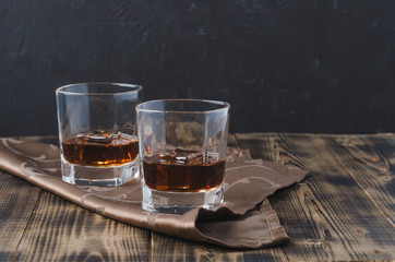 Two Glasses of whiskey with ice cubes on a wooden table/Two Glasses of whiskey with ice cubes on a wooden table. Black background with copyspace.