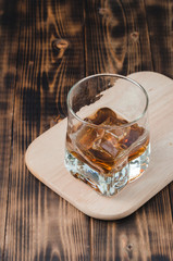 Glass of cognac with ice cubes on a wooden table/Glass of cognac with ice cubes on a wooden table. Top view.