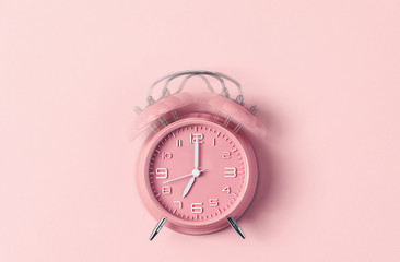 Classic pink alarm clock ringing at seven o'clock against pastel pink background - obrazy, fototapety, plakaty