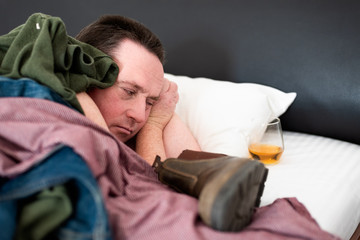 Drunk middle-aged man in messy bed with alcohol