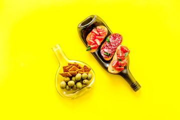 Snack set on wine bottles on yellow desk from above