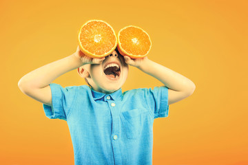 Happy cute boy is having fun played with fruit orange on yellow background wall. Bright photo of a...