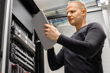 Fototapeta premium Male IT Technician Holding Digital Tablet Analyzing Servers in Datacenter