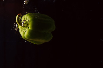 fresh green bell pepper in water with splash on black background