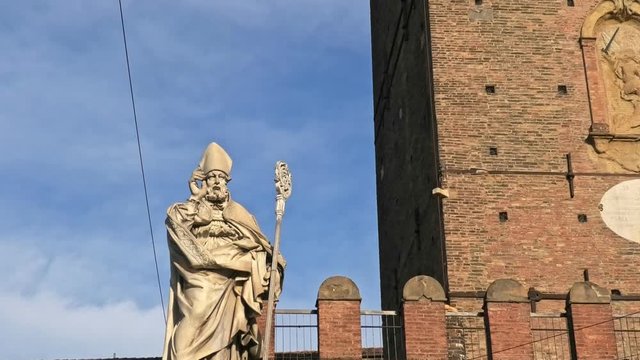 San Petronio statue, patron of Bologna with Two Towers building, symbol of city in blue sky, Italy. Asinelli tower and Garisenda tower in historic downtown with clock tower of city.