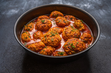 Homemade meatballs in tomato sauce with herbs in a saucepan on a dark wooden background