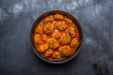 Homemade meatballs in tomato sauce with herbs in a saucepan on a dark wooden background. Top view