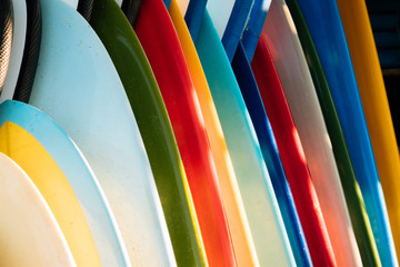 Close up Set of different color surf boards in a stack on sandy beach for rent. Multicolored surfboards as rainbow.