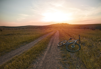 Mountain bike lies on the ground during beautiful sunset on the horizon. Mountain bicycle