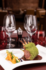 Piece of lamb rack with bone roasted with green herb, bread, sweet potatoes puree, baby vegetables