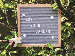 Love your garden. Gardening concept with felt letter board in the branches of an dwarf apple tree with blossom flowers and green foliage. Selective focus view with blurry background and copy space.