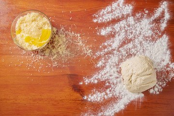 Grated cheese with an egg in a plate and sprinkled flour with stocked dough on a wooden table before cooking, top view