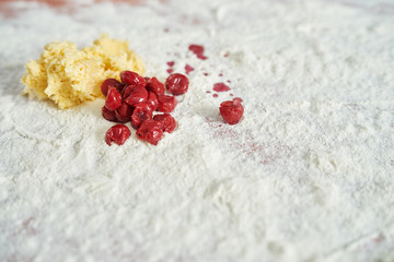 Obraz na płótnie Canvas Pieces of ready-made tasty dough with grated cheese and red cherries lying on a wooden kitchen table covered with flour