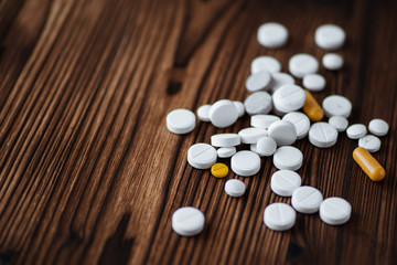 Medicine white and yellow pills or capsules on wooden background.