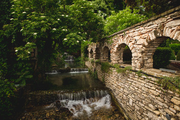 Fototapeta na wymiar Small waterfall in green environment and brick stone wall