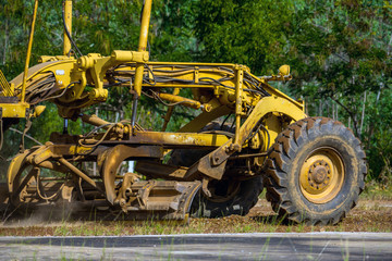 Close up of Motor grader clearing and leveling construction site surface. Grader industrial machine on road construction work.