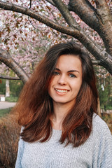 A girl with long hair walks in a blooming garden, spring blooming pink cherry trees, close-up portrait