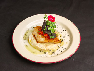 Appetizingly fried piece of fish on a pillow of mashed potatoes decorated with microgreens on a dark background