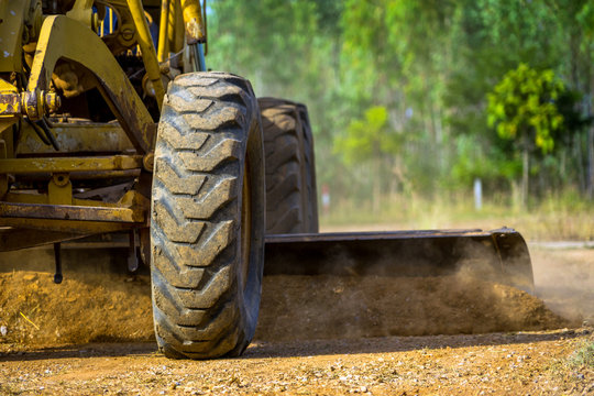 Close up of Motor grader clearing and leveling construction site surface. Grader industrial machine on road construction work.