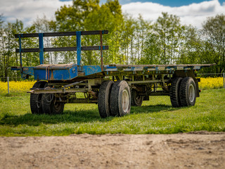 Ein zweiachsiger blauer Anh&auml;nger aus der Landwirtschaft auf einer gr&uuml;nen Wiese