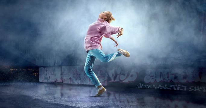 Female street dancer in a action with a graffity wall behind the fog on a backgroung.