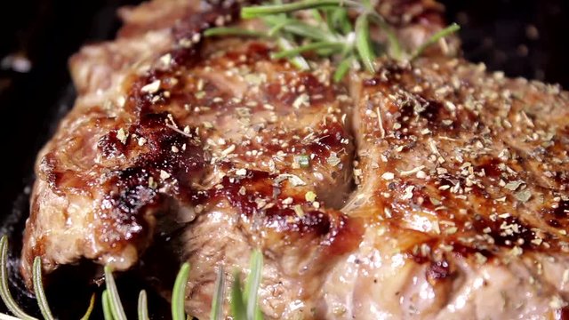 Grilling beaf steak. Cooking and pouring rosemary flavour on meat. Delicious food preparation.