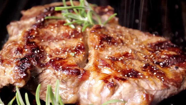 Grilling beaf steak. Cooking and pouring pepper on meat.  Delicious food preparation.