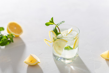 Lemonade with lemon, mint and ice cubes in glass on white stone background. Cold summer refreshing drink or beverage. Summer Menu, recipe. Cold detox water with lemon