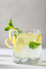 Refreshing lemonade with lemon, mint, ginger and ice in glass and bottle on white concrete background. Summer refreshing drink. Cold detox water with lemon. Close up. Menu