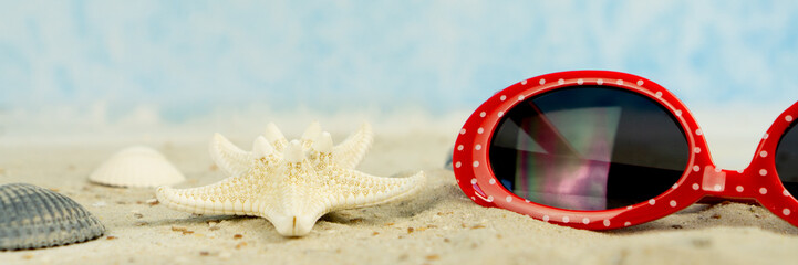 A red sunglasses with white dots in the sand, with shells and starfish, panorama