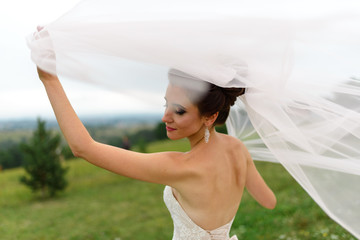 Portrait of a bride under a veil. The wind blows up a veil. A woman is standing with her back. Close-up