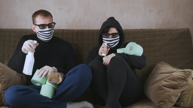 Man and woman on the couch in protective masks.