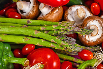 Green asparagus surrounded by various fresh raw vegetables like bell pepper, tomatoes and mushrooms