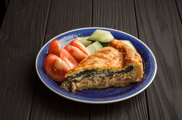 Horizontal image, Flat-lay, of vegetable pie with spinach and salmon on blue plate from above on a textured black background.