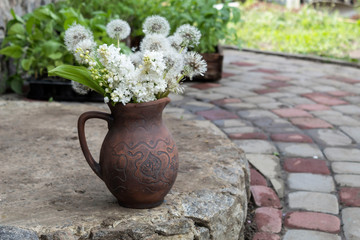On the porch in a pot of red clay is an airy bouquet of balloons of dandelion seeds and white lilac. In the background are boxes of seedlings.