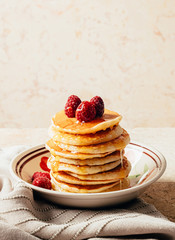 Pancakes poured with honey decorated with raspberries on a plate on a beige background. Copy space