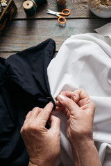 Female hands stitches black and white fabric on wooden table, scissors, casket, thread, glasses