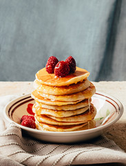 Pancakes poured with honey decorated with raspberries on a plate on a blue background. Copy space